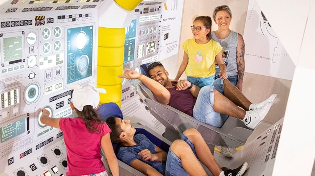 Des visiteurs essayent les sièges d'une capsule de décollage dans le cadre des animations proposées dans la file d'attente de l'attraction Objectif Mars