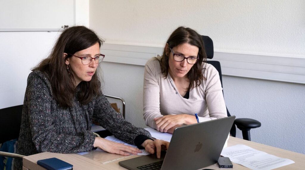 Deux jeunes femmes travaillent ensemble dans un bureau, face à un écran d’ordinateur portable.
