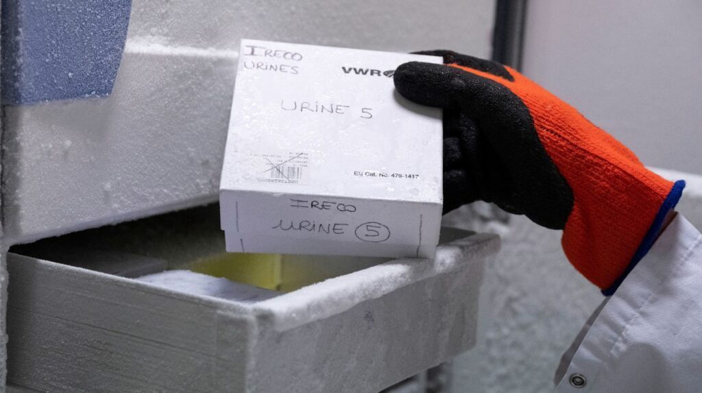 Une main gantée sort une boîte en carton d’un tiroir de congélateur de laboratoire.