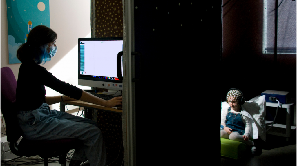 Une chercheuse à son ordinateur, avec un enfant équipé d’un bonnet d’électrodes qui permet de suivre son activité cérébrale.