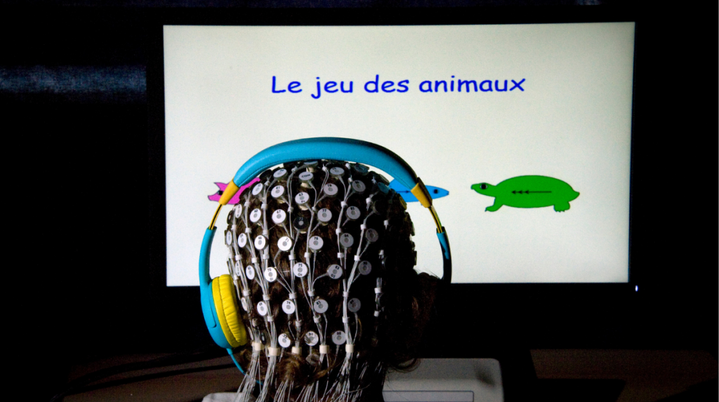 Un enfant de dos. Équipé d’un bonnet d’électrode, il fait face à un écran avec un jeu vidéo